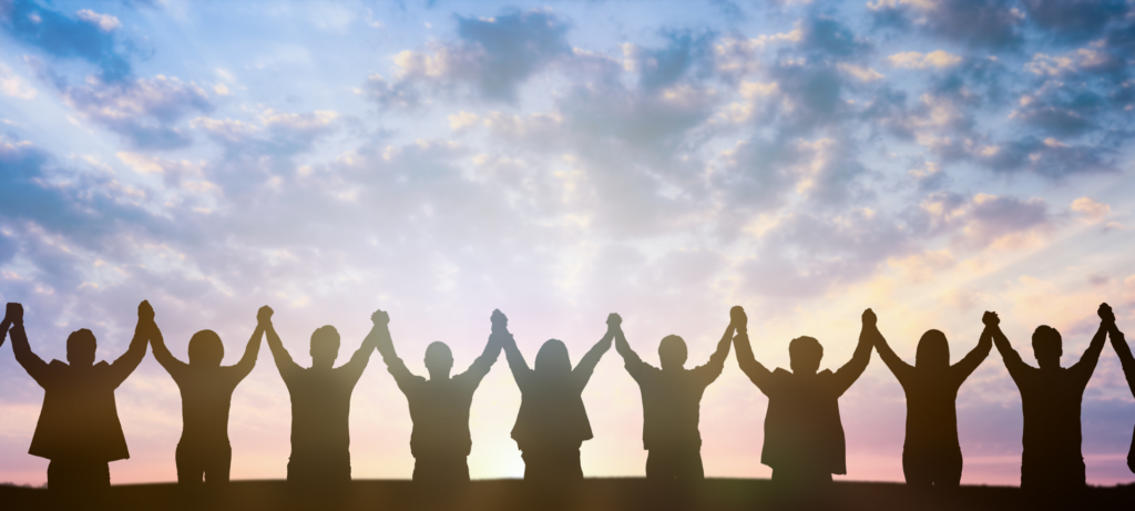 Photo of the silhouettes of individuals holding hands in the air towards the clouds.