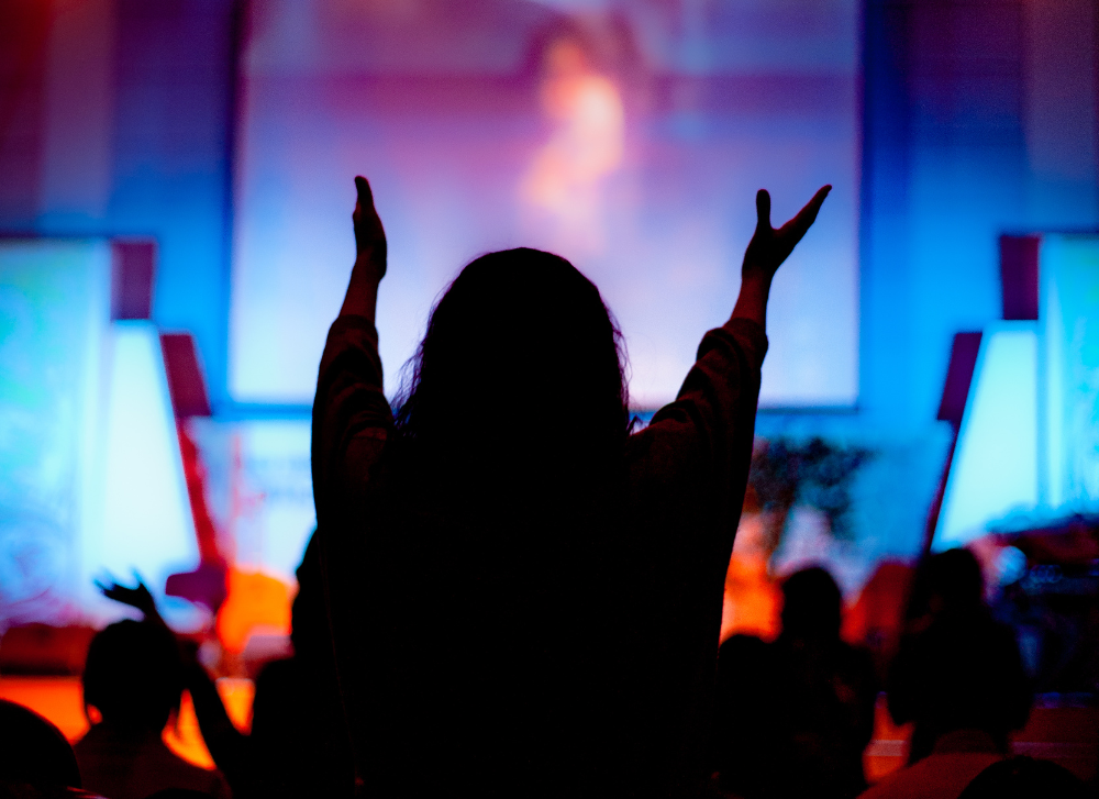 Photo of a silhouette of an individual worshiping with her hands outstretched upward.